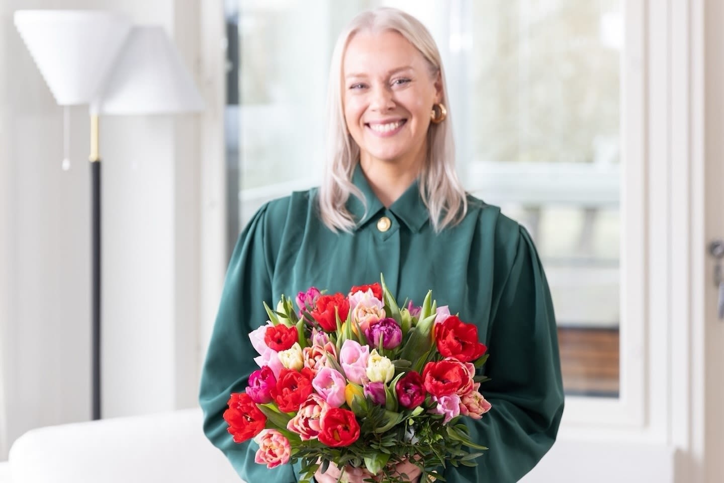 Hymyilevä henkilö vihreässä paidassa pitää kaunista tulppaanien kukkakimppua, jossa on punaisia ja vaaleanpunaisia kukkia.