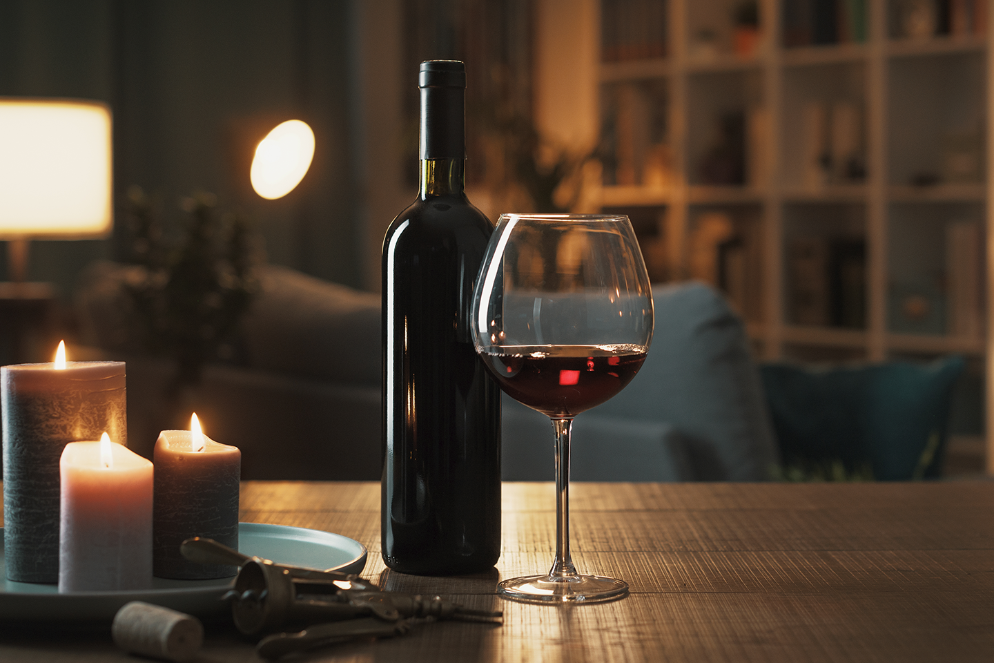 Tunnelmallinen ilta punaviinin äärellä – pöydällä viinipullo, lasi, kynttilöitä ja pullonavaaja kodikkaassa valaistuksessa.