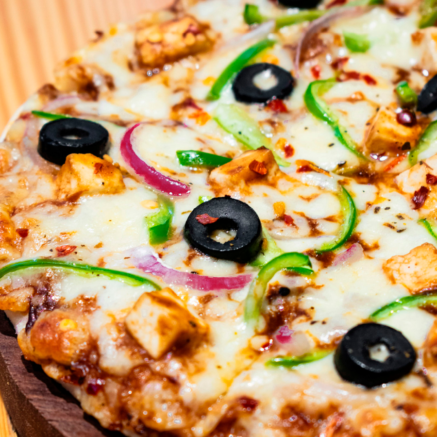 Herkullinen pizza täynnä sulatetun juuston peittämiä täytteitä: mustia oliiveja, vihreää paprikaa, punasipulia ja kanaa.