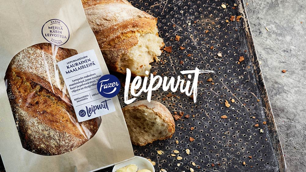 Rapean kuorinen Fazerin maalaisleipä pakkauksessaan leipäpellillä, vieressä leivästä leikattu pala ja Leipurit-logo.
