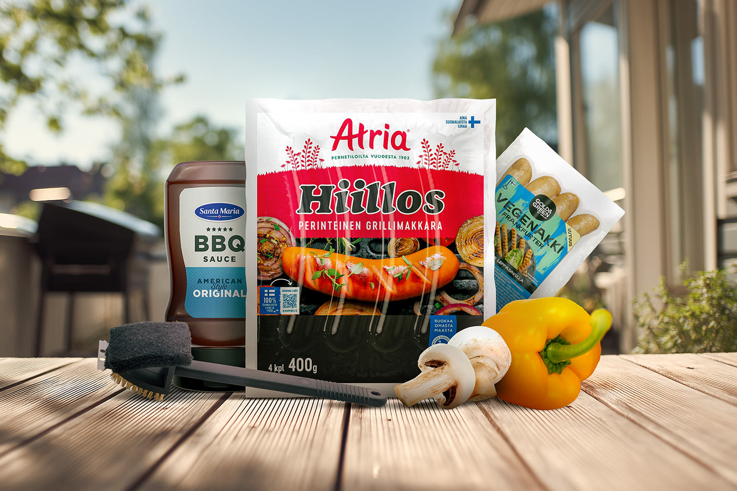 Aurinkoisella terassilla grillaustuotteita: Atrian Hiillos-makkarat, BBQ-kastike, sieniä ja keltainen paprika grillausta varten.