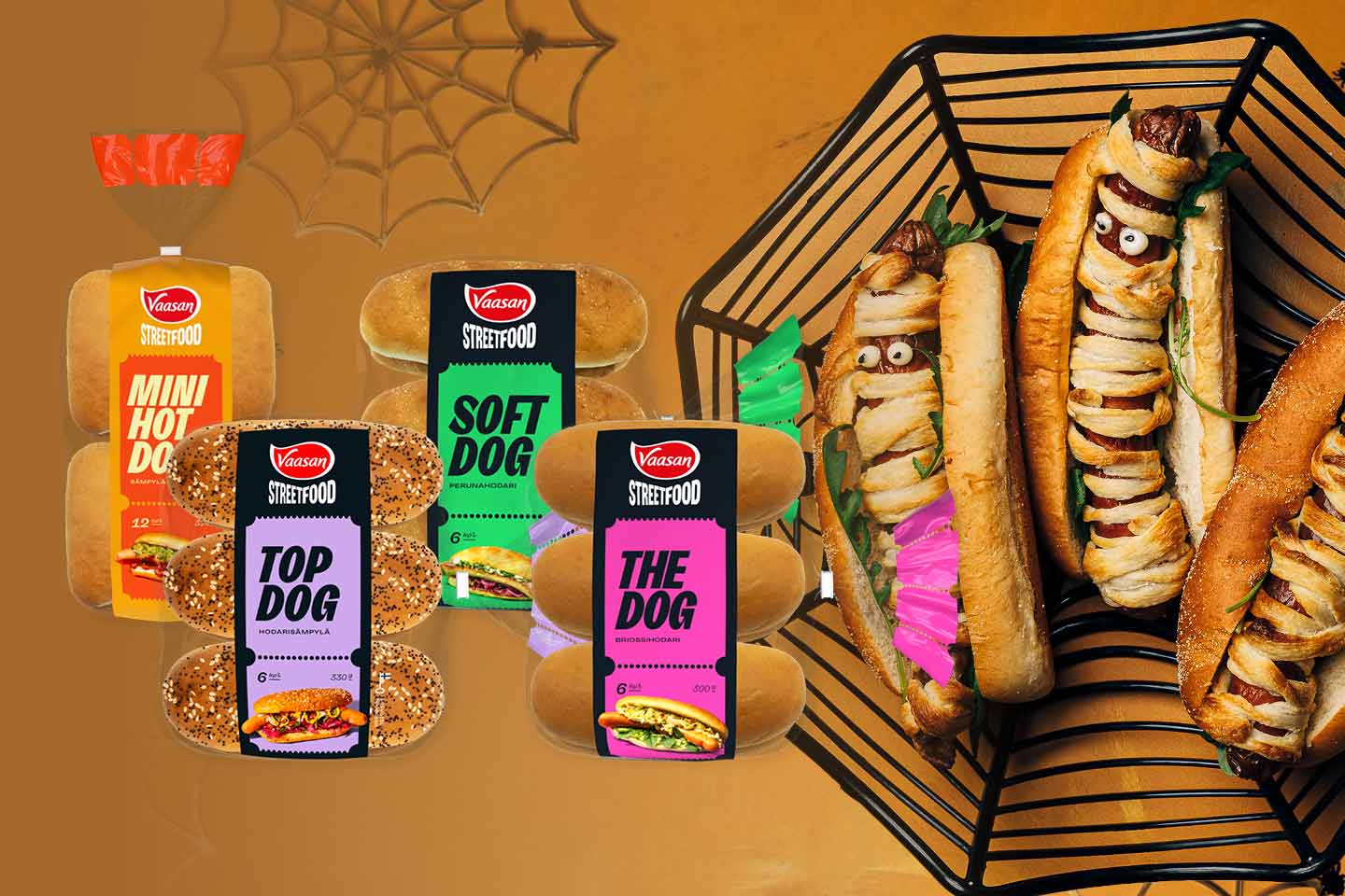 Vaasan Street food -hodarisämpyläpakkauksia ja halloween-henkisiä muumio-hotdogeja lautasella oranssia taustaa vasten.