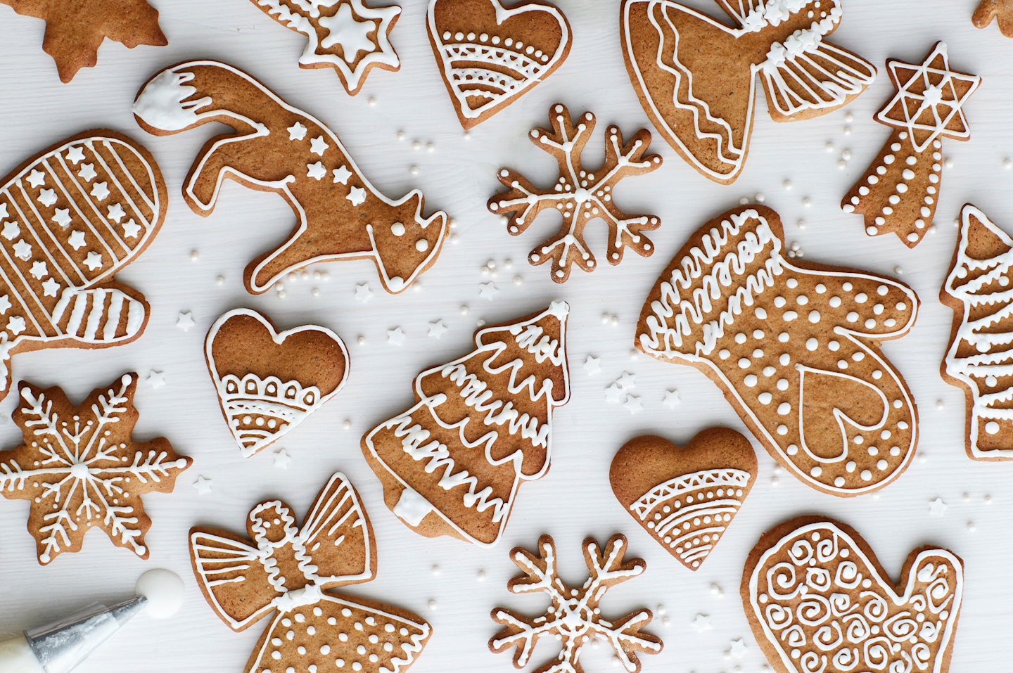 Kauniisti koristeltuja jouluisia piparkakkuja valkoisella taustalla - sydämiä, tähtiä, kuusia ja lumihiutaleita.