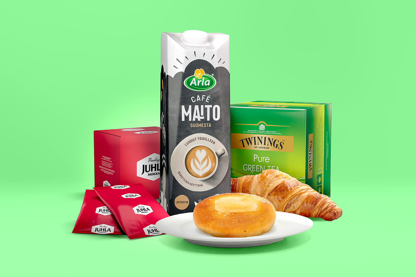 Arla Café Maito, Paulig Juhla Mokka, Twinings vihreä tee, donitsi ja croissant vihreää taustaa vasten.