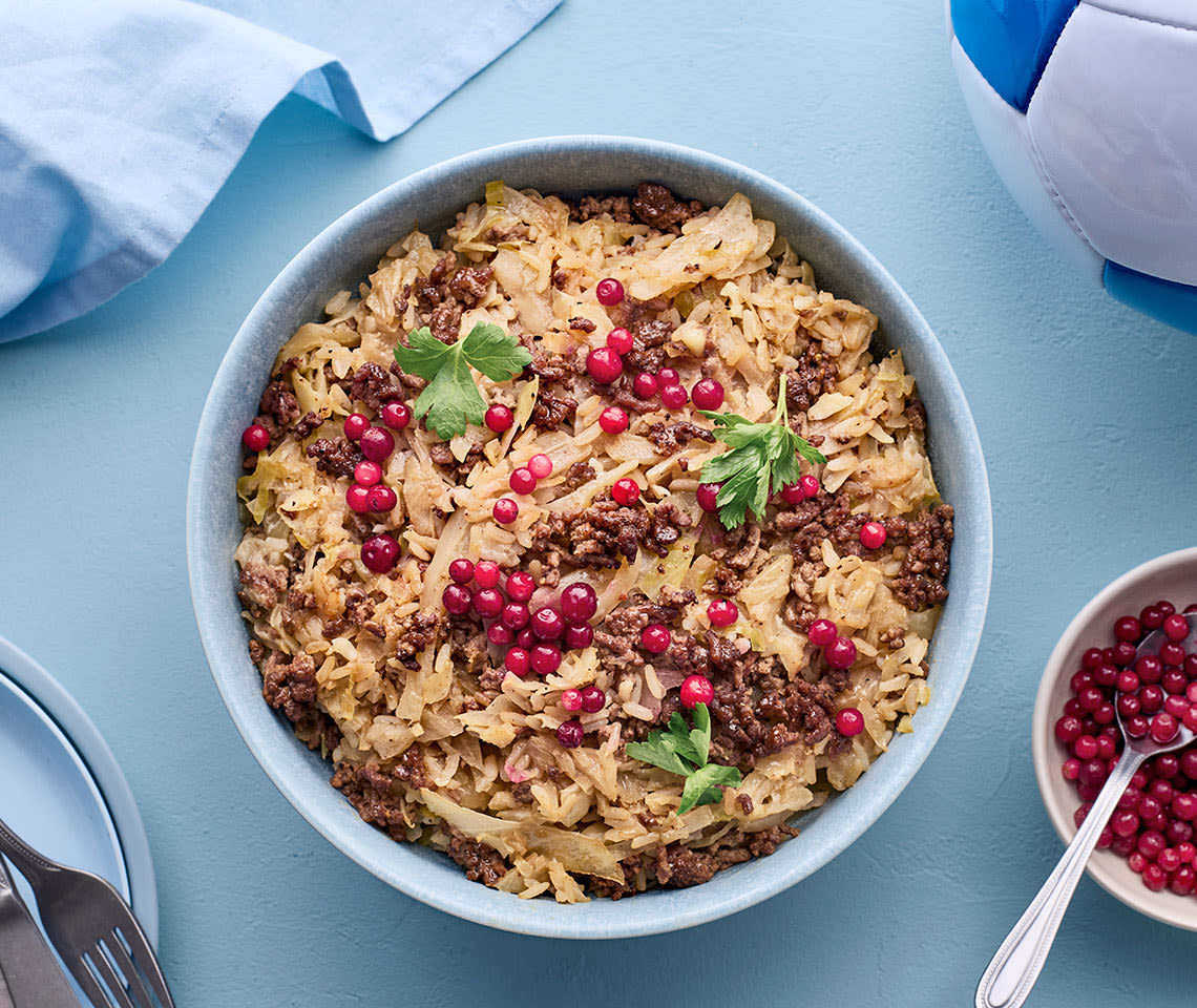 Kaalipata pyoreässä padassa, jonka päällä puolukoita. Kuvan laidassa jalkapallo.