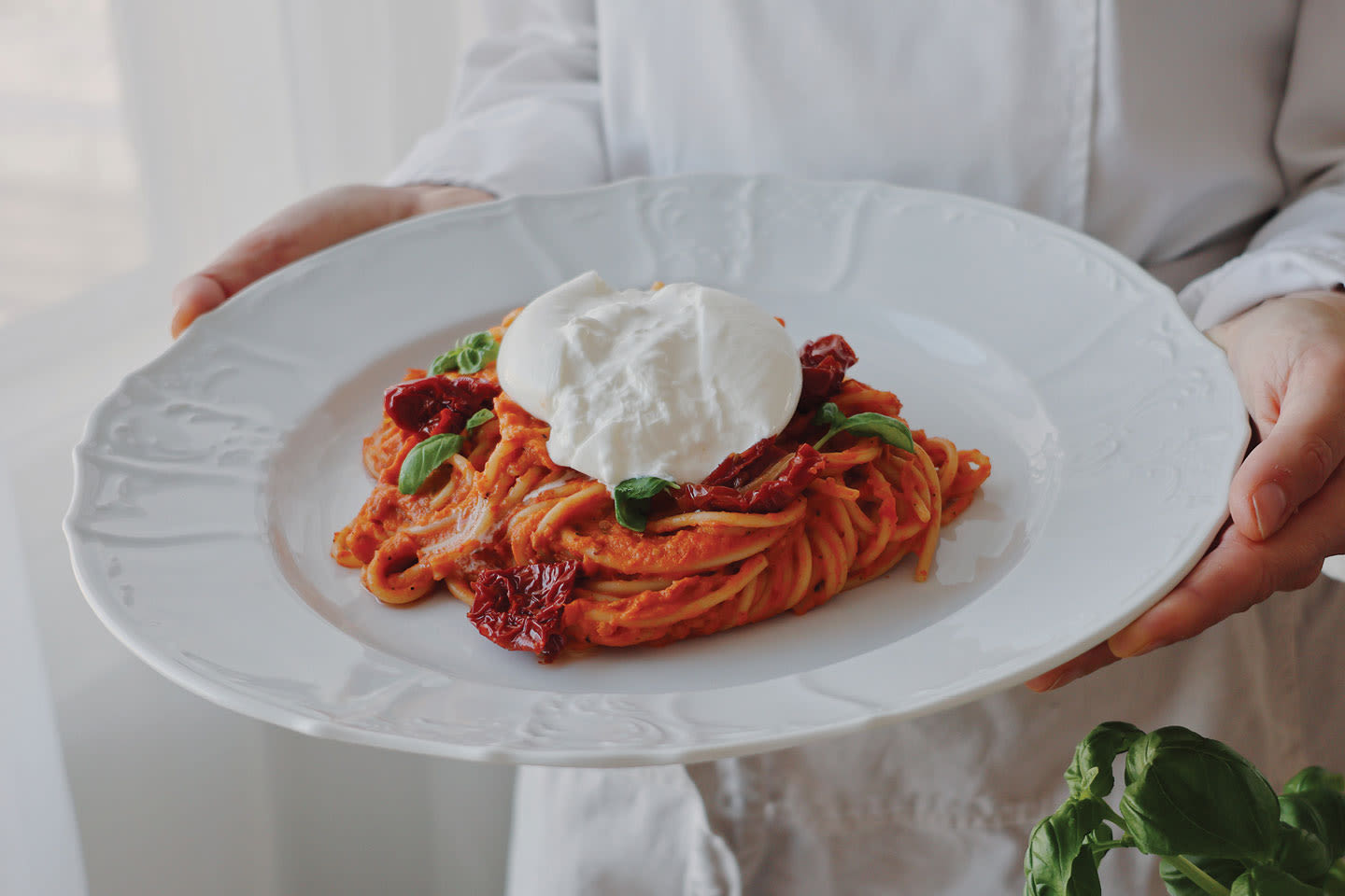 Herkullinen pasta-annos valkoisella lautasella, jossa tomaattikastiketta, tuoreita yrttejä ja pehmeä mozzarellapallo päällä.