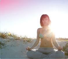 Bilde av en kvinne som sitter på stranden og mediterer. Bildet viser, att det går an å slappe av og leve som vanlig, også når du har menstruasjon.