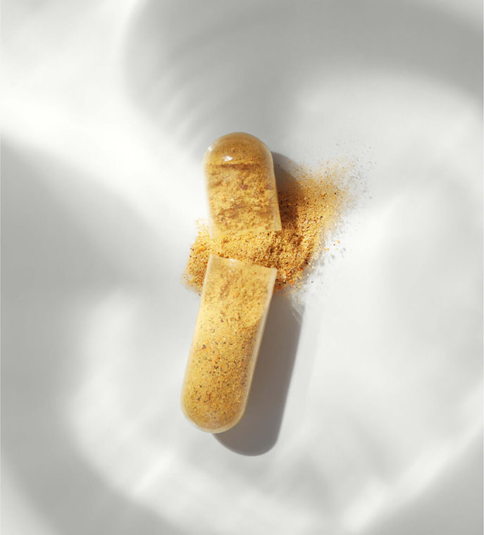 A yellow Nutrafol capsule broken in half, with powder spilling out onto a white shadowed background.