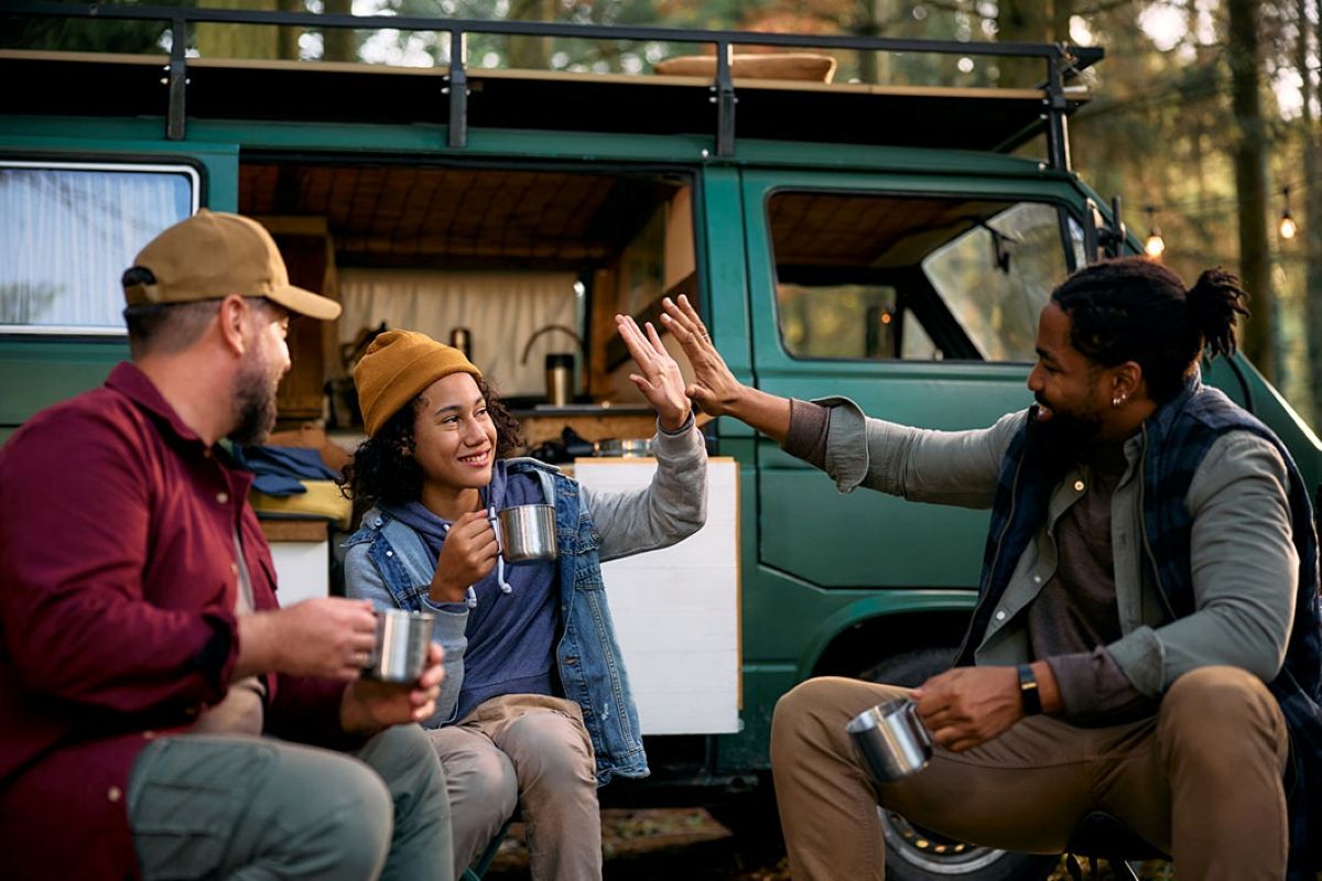 A young girl gives her father a high five as they sit outside a camper van.
