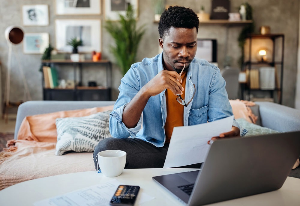 Picture of man working on his taxes in his living room. He's gathering IRS forms to note his HealthEquity HSA contributions.