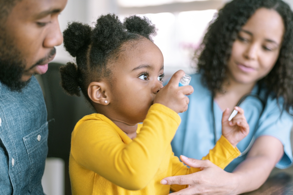 dad holding child using asthma inhaler as nurse looks on