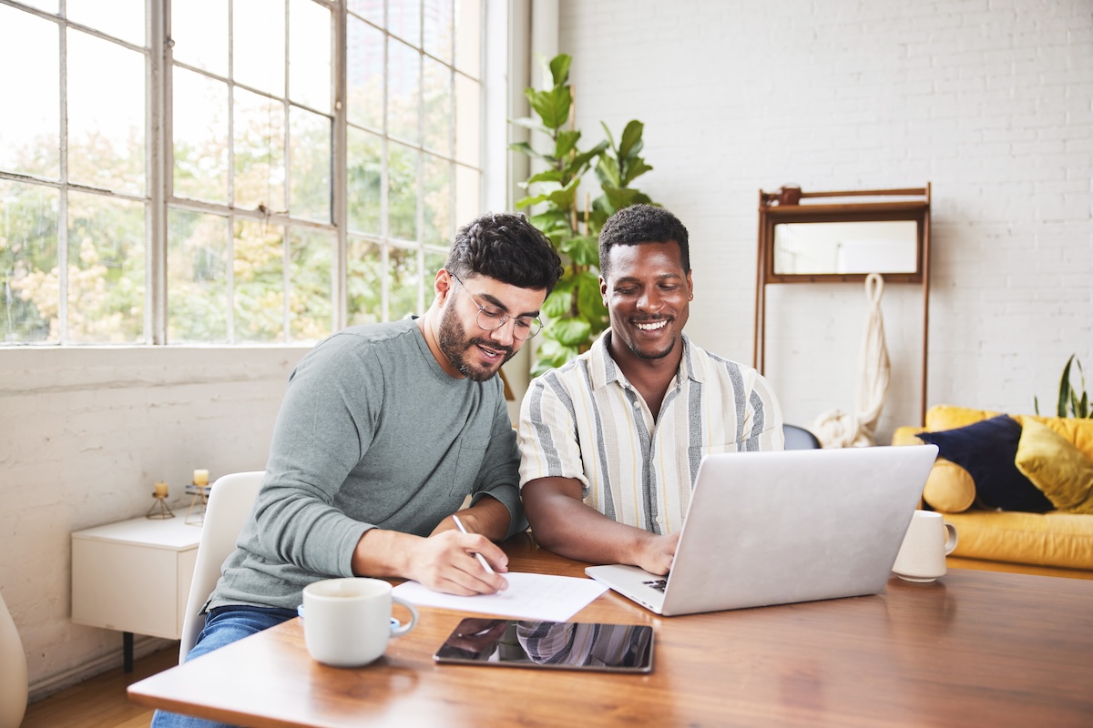 Two men seated at a table together looking at laptop and determining how much they should contribute to their HealthEquity Health Savings Account. 