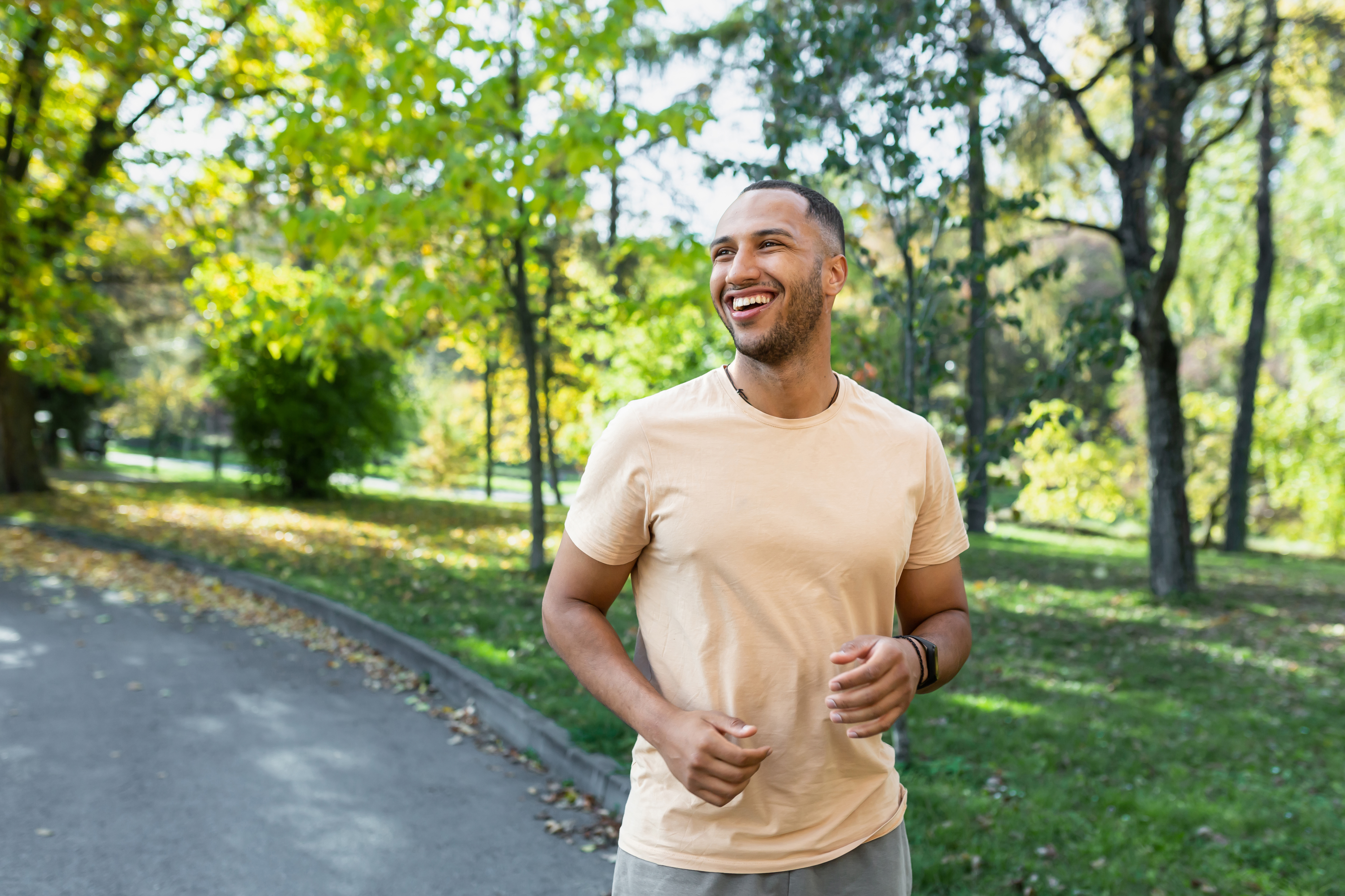 A man smiles as he runs through the park.
