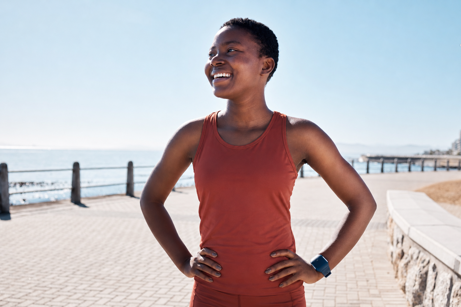 A smiling woman stands confidently on a pathway along the coast.