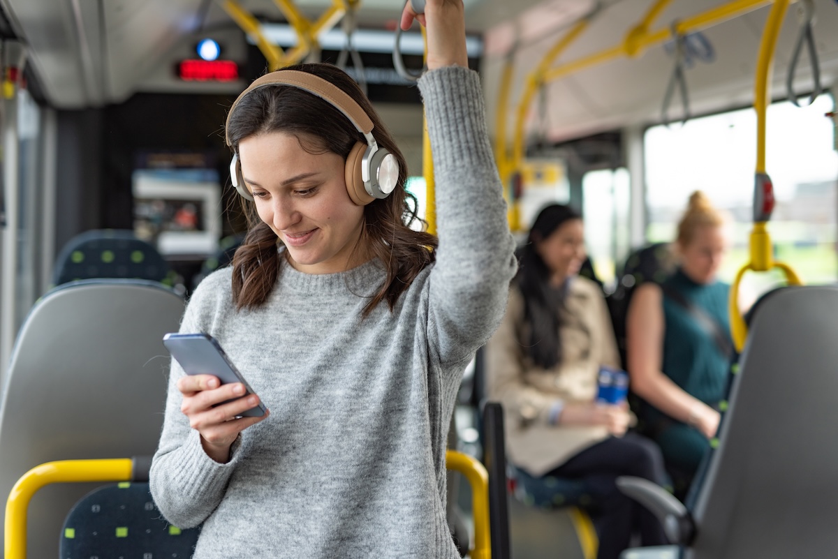 woman with headphones listening to something on phone standing on a bus commuting to work