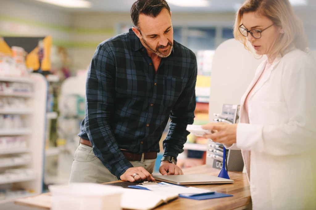 Adobe Stock Photo of man in plaid shirt receives instruction from Pharmacist at pharmacy counter for his medication question