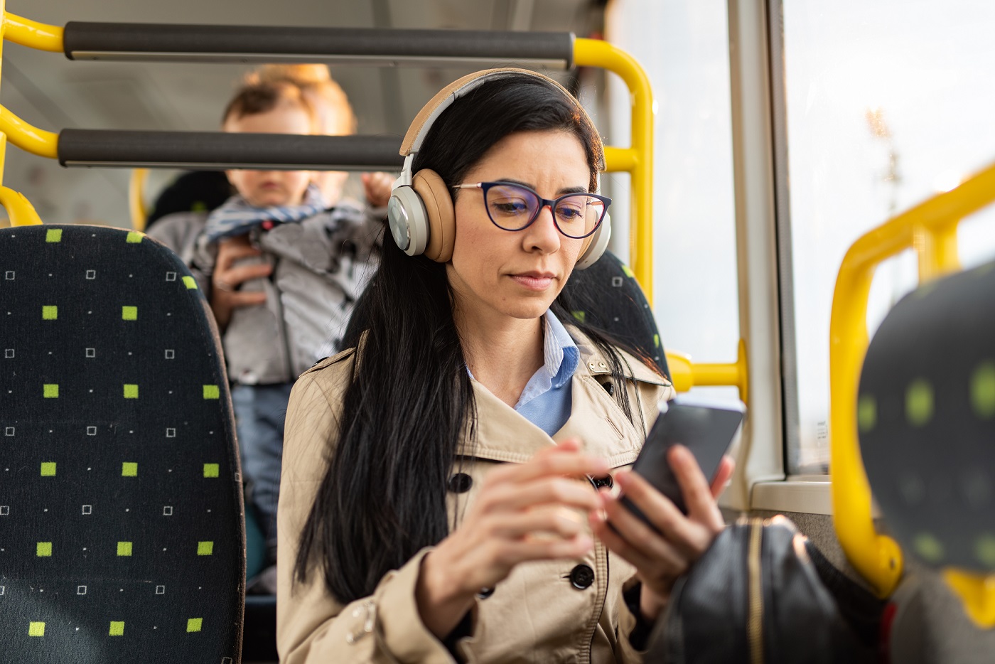 Picture of young, professional woman listening to music and browsing her smartphone while commuting on a bus.