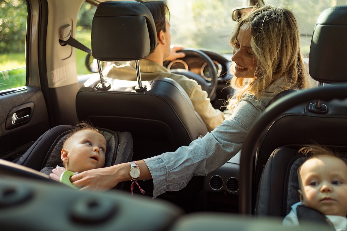 woman in car looks back at twins in car seats while man is driving