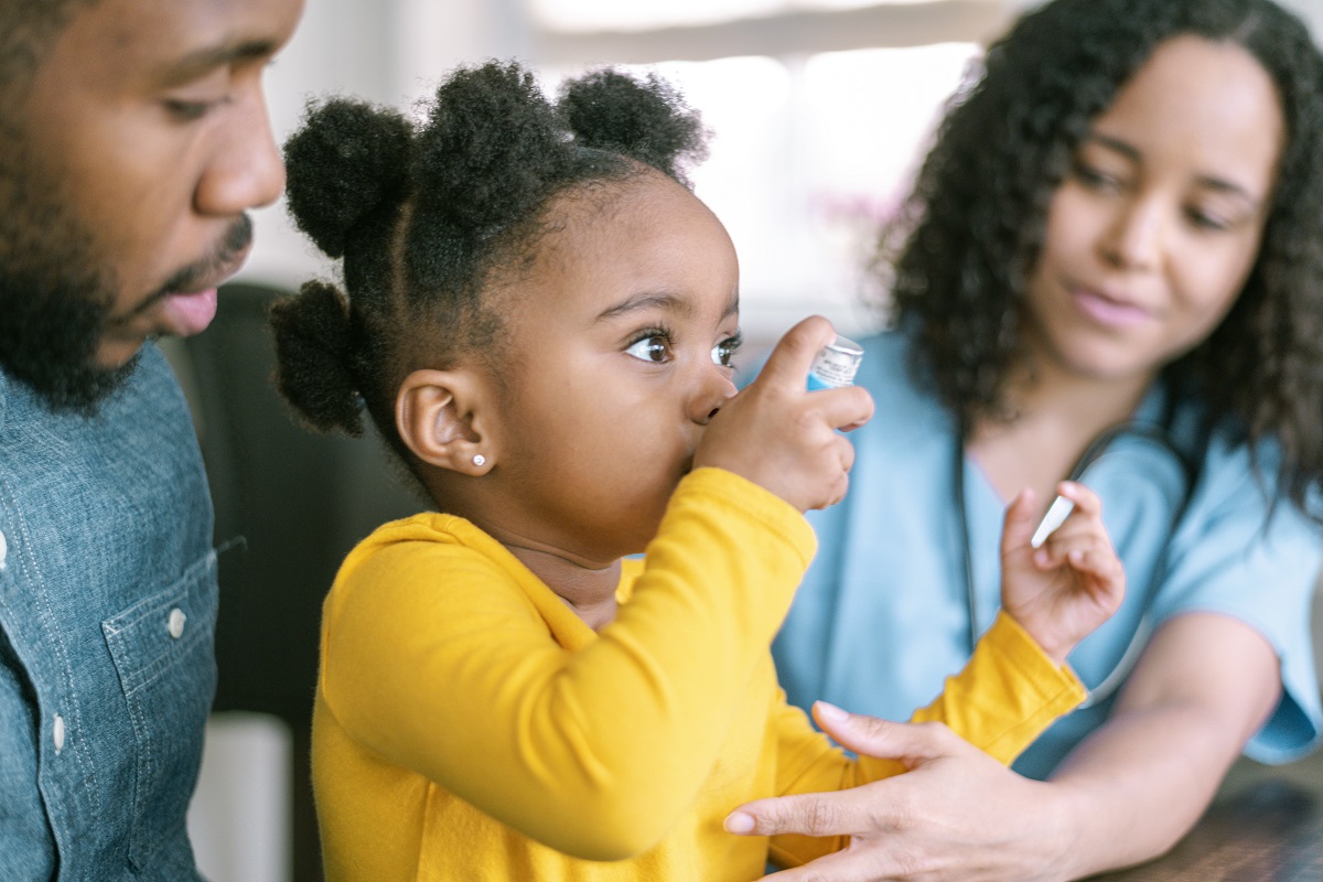 Photo of medical professional meeting with a father and young daughter. Young girl is using an inhaler.