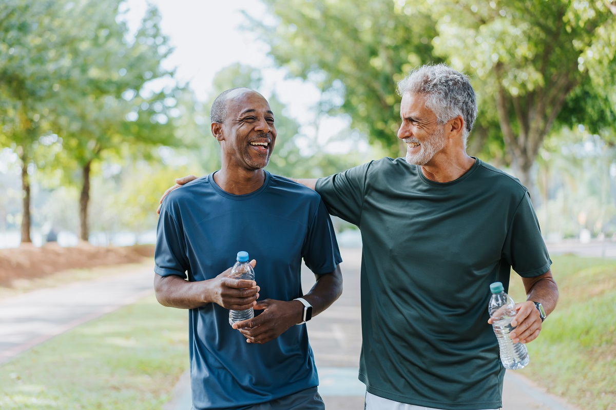 Picture of two men walking outside after exercising. They are drinking water and smiling.
