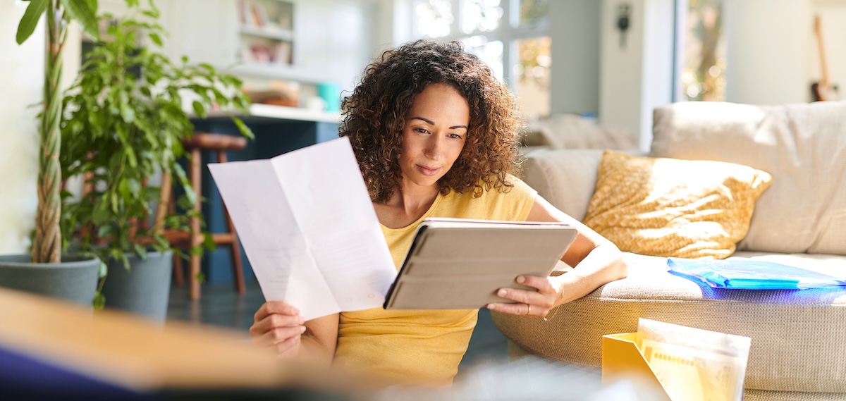 woman in comfortable living room looking at ipad and paperwork