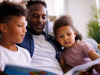 Father reading a book with two children at home, representing the peace of mind and protection that insurance provides for families.