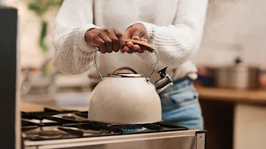 Person boiling a kettle on a gas stove in a kitchen, representing everyday household energy use and gas consumption.