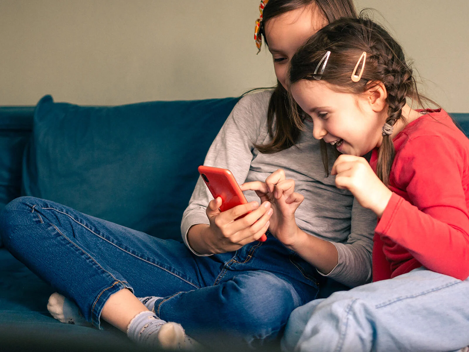 Two children using a smartphone together at home, representing family mobile plans that help keep everyone connected.