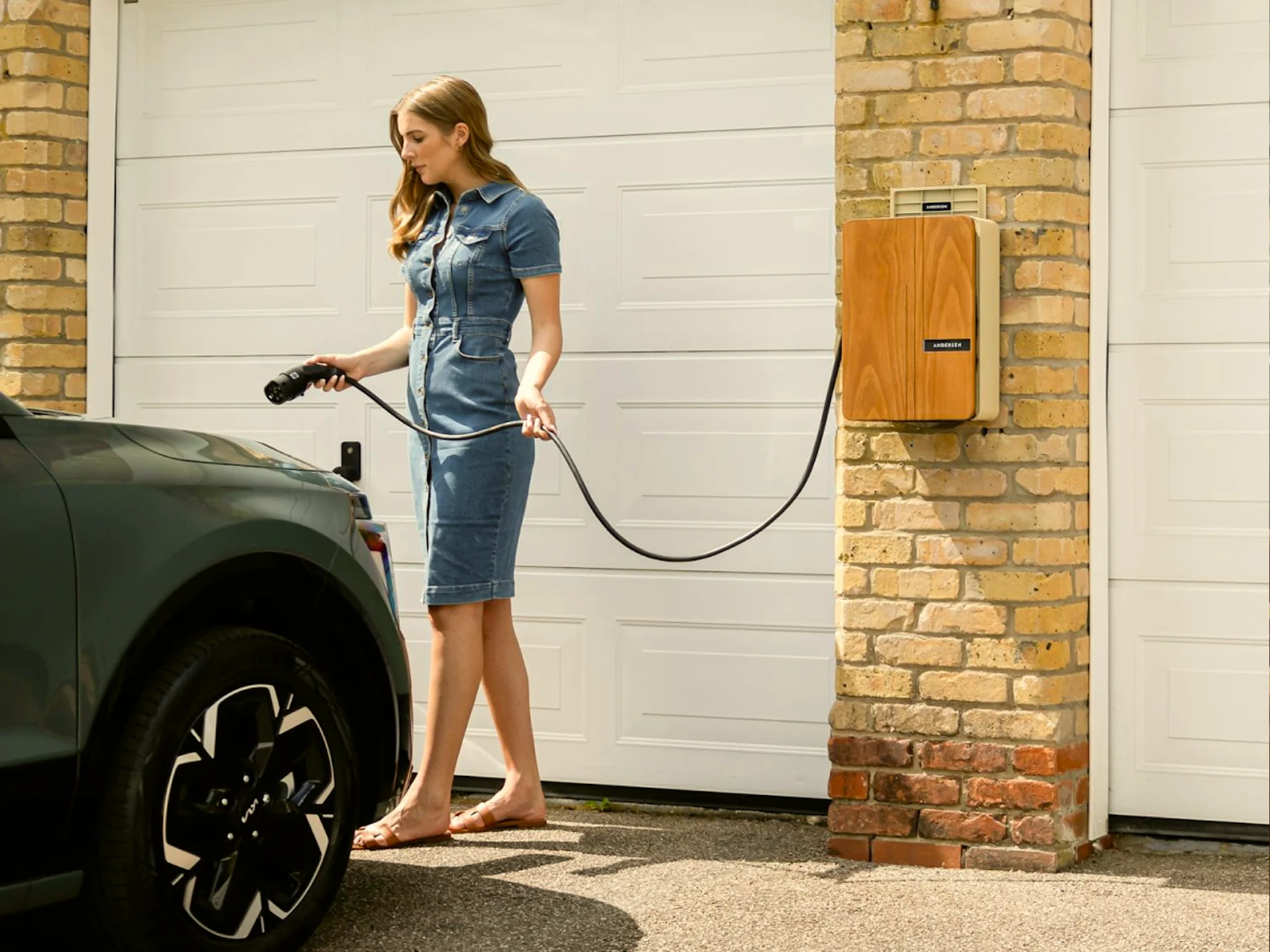 A person connects an electric vehicle to a home charging point outside a house, representing convenient home EV charging and electric vehicle ownership.