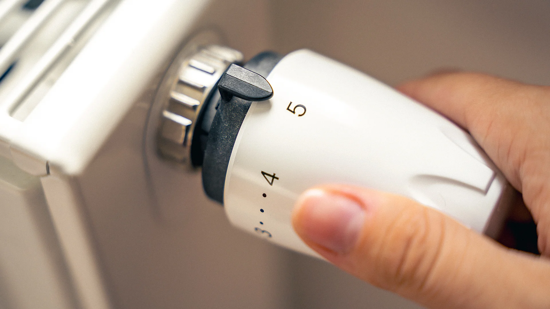 Hand adjusting a radiator thermostat to increase the heating temperature