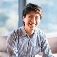 Smiling Asian man in checkered shirt sitting on couch near bright window