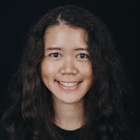 Young girl with long dark wavy hair smiling at camera against black background in portrait photo