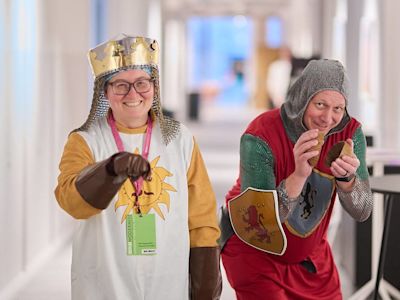Two people in medieval costumes posing in a bright hallway, one dressed as a king in gold and white, the other as a jester.