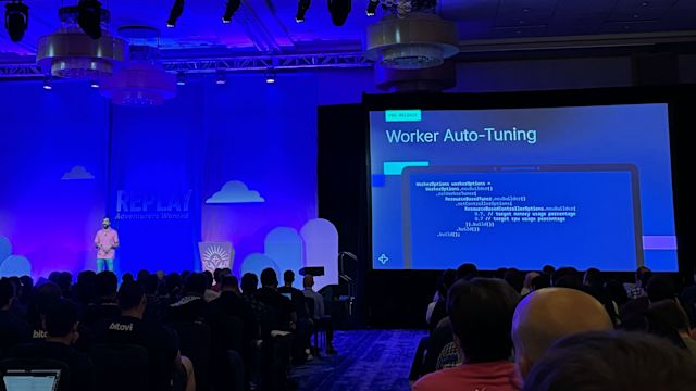 Tech conference presentation showing Worker Auto-Tuning code on large screen with blue lighting and audience viewing.