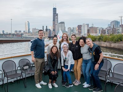 Group of eight people posing on a boat deck with Chicago skyline and Willis Tower in the background.