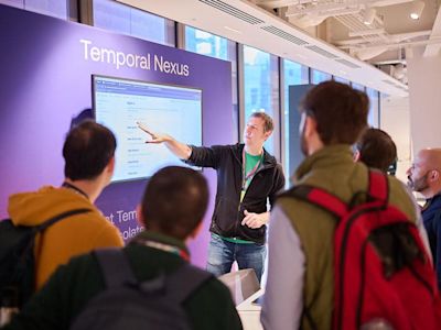Presenter in black jacket pointing at screen displaying Temporal Nexus to audience in modern office space