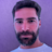 Man with dark hair and beard wearing white t-shirt against purple background