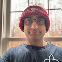 Person wearing glasses and a red San Francisco 49ers knit beanie, smiling in front of a window with autumn foliage visible.