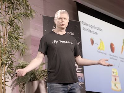 Man in black Temporal t-shirt presenting at tech conference with slide showing CakePHP application architecture