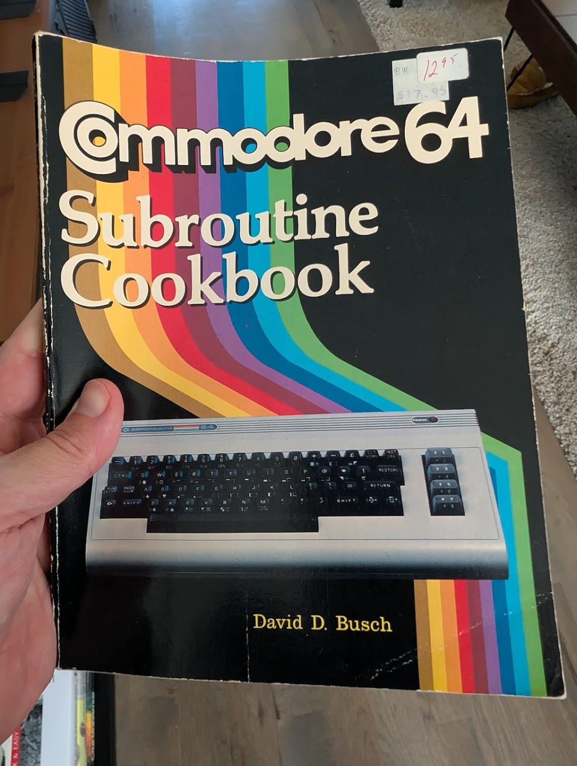 A hand holding a copy of the Commodore 64 Subroutine Cookbook by David D. Busch