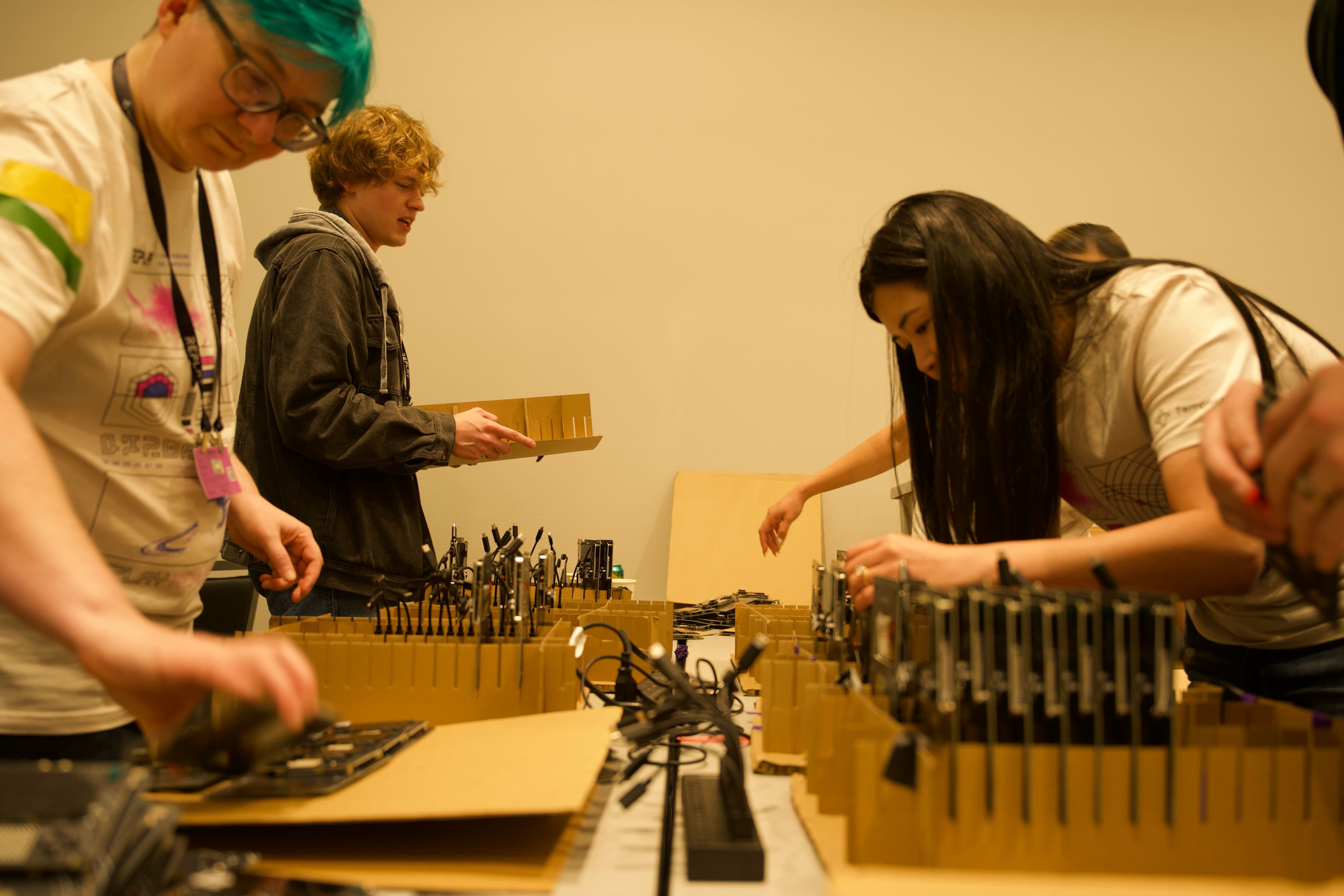 Tim, Angela, and Angie at the charging station of the Replay 2026 badge assembly line