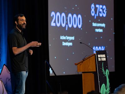 Speaker presenting statistics on screen showing 200,000 Active Targeted Developers and 8,753 Astronomy nerds at podium.