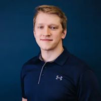 Professional headshot of a young man with light brown hair wearing a navy blue polo shirt against a dark blue background.