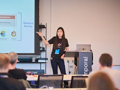 Woman presenting technical architecture diagram showing Frontend Service, Backend Services, and Temporal Service to audience.
