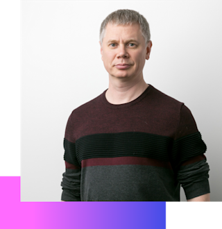 Man with short gray hair wearing a color-blocked sweater in burgundy, black, and gray against a white background.