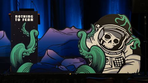 Stage display with astronaut skull artwork and green tentacles, purple mountain backdrop, and podium reading Nothing to Fear.