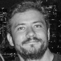 Black and white portrait of a smiling bearded man with city lights in the background at night
