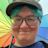 A nerd with glasses and blue hair smiling and holding a rainbow umbrella
