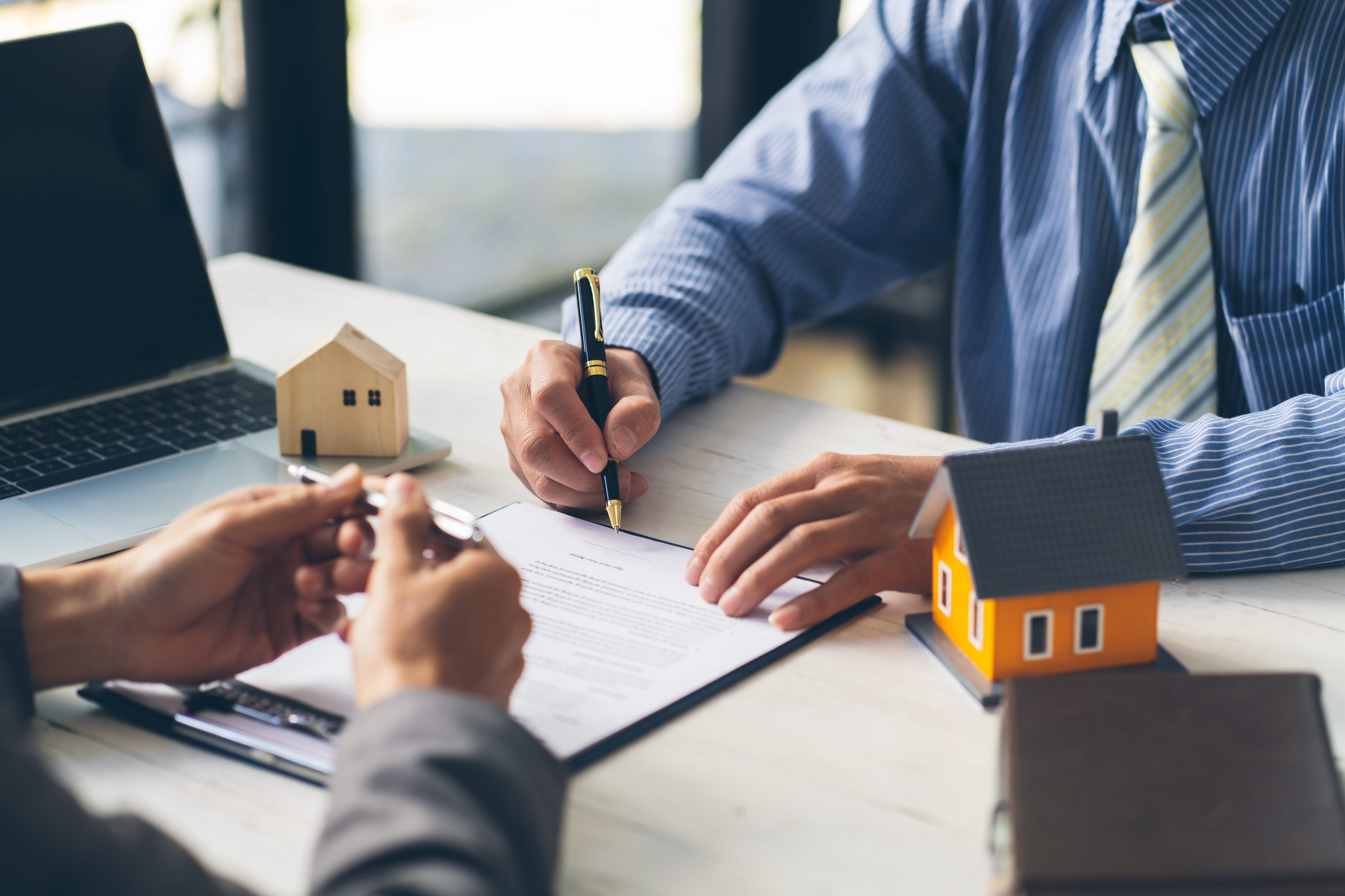 2 people meeting with a note pad and mini houses 