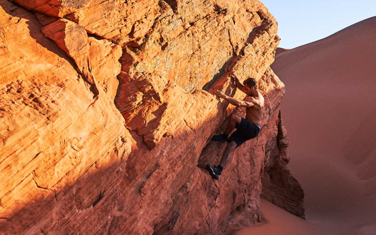 St. George (Greater Zion) | Photo Gallery | 9 - Man bouldering on rock wall by sand dunes in southern Utah.